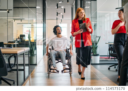 A business leader with her colleague, an African-American businessman who is a disabled person, pass by their colleagues who work in modern offices A business leader with her colleague, an African-American businessman who is a disabled person, pass by their colleagues who work in modern offices 114573170