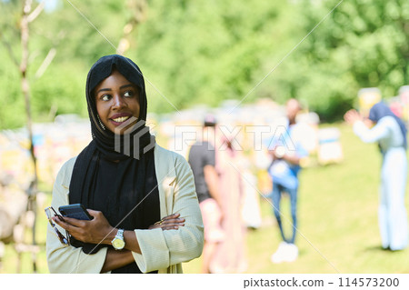 Empowered Middle Eastern Muslim Woman in Hijab Balances Modern Technology and Traditional Beekeeping Business 114573200