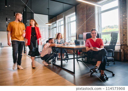 A diverse group of business professionals collaborates in a modern startup coworking center, utilizing a mix of paper-based and technological tools such as mobile phones and computers  114573908