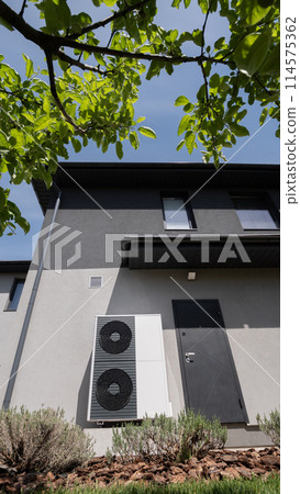 A modern cottage's wall accommodates the outdoor unit of a heat pump. 114575362