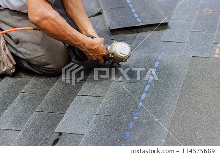 New asphalt bitumen shingles are being installed by roofer using pneumatic air nail gun 114575689