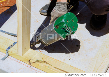 Framer worker installing beams using air nails hammer in nailing wooden frame Framer worker installing beams using air nails hammer in nailing wooden frame 114575715
