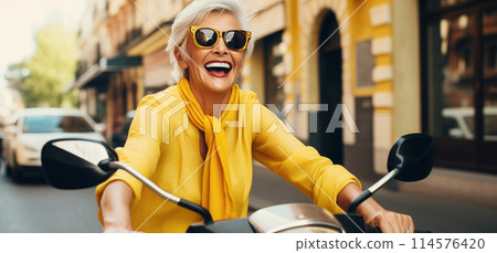 Cheerful happy senior woman riding scooter on city street, stylish elderly female driving moped 114576420