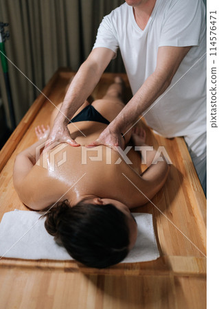 Vertical shot of relaxation woman back massage with masseur in cosmetology spa salon. Relaxing female client getting service aromatherapy massage with masseuse in wellness center with dark interior. 114576471