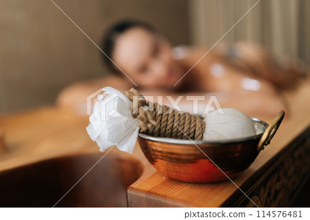 Closeup selective focus shot of Ayurveda massage powder pads on blurred background of lying female client. Close-up of Ayurvedic Treatment Kizhi from Kerala, effective Ayurvedic rejuvenation treatment 114576481