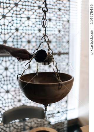 Vertical cropped shot of unrecognizable specialist pouring hot aromatic oil into bowl during preparation for exotic Shirodhara treatment, Ayurvedic healing technique in wellness center. Vertical cropped shot of unrecognizable specialist pouring hot aromatic oil into bowl during preparation for exotic Shirodhara treatment, Ayurvedic healing technique in wellness center. 114576486