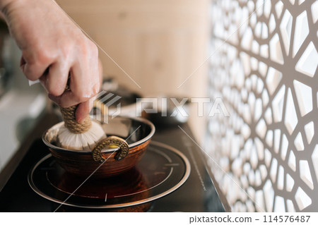 Close-up hands of unrecognizable ayurvedic massage practitioner dipping cotton-wrapped herbal bundle into aromatic oil during prepare to Shirodhara treatment. Tranquil and serenity at spa salon. Close-up hands of unrecognizable ayurvedic massage practitioner dipping cotton-wrapped herbal bundle into aromatic oil during prepare to Shirodhara treatment. Tranquil and serenity at spa salon. 114576487