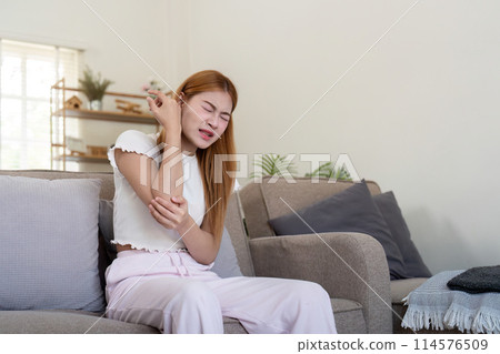 Young woman feeling pain in her elbow while sitting indoors 114576509