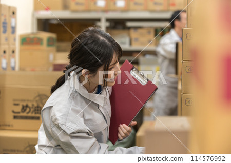 一名身穿工作服的年輕女子在倉庫檢查產品 一名身穿工作服的年輕女子在倉庫檢查產品 114576992