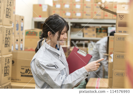 一名身穿工作服的年輕女子在倉庫檢查產品 一名身穿工作服的年輕女子在倉庫檢查產品 114576993