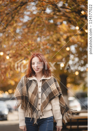 A delightful redhead smiles brightly, adding a touch of happiness to the autumn streets. 114577022