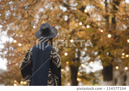 A stunning young woman, channeling bohemian vibes, dons a black hat in the autumn city streets. 114577104