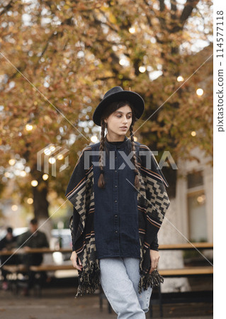 A captivating girl, with bohemian flair, accents her look with a black hat in the fall cityscape. A captivating girl, with bohemian flair, accents her look with a black hat in the fall cityscape. 114577118