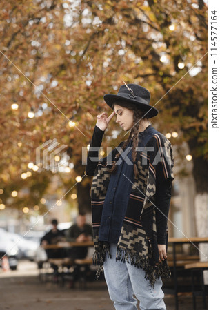 A radiant lady, embracing boho vibes, pairs her look with a black hat while exploring the autumn cityscape. 114577164