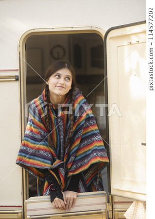 A beautiful girl in a hippie ensemble poses against the backdrop of a trailer in the park. A beautiful girl in a hippie ensemble poses against the backdrop of a trailer in the park. 114577202