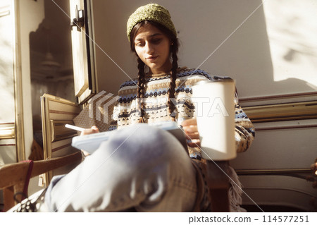 A fashionable lady embraces her hippie persona against the natural beauty of the park, with a trailer nearby. A fashionable lady embraces her hippie persona against the natural beauty of the park, with a trailer nearby. 114577251