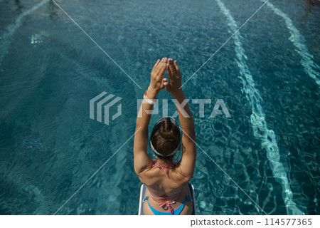 A captivating girl in a bathing suit sits by the pool, her back against the edge. A captivating girl in a bathing suit sits by the pool, her back against the edge. 114577365