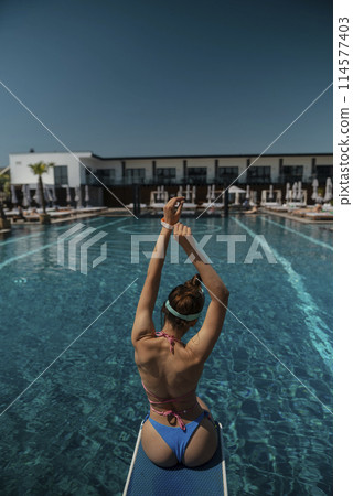 A lovely woman in a swimsuit sits by the pool, facing away from the pool. A lovely woman in a swimsuit sits by the pool, facing away from the pool. 114577403