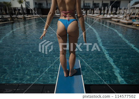 An elegant woman with a lovely figure lounges by the pool, dressed in a bikini. 114577502