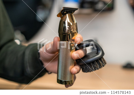 Hairdresser holding trimmer and brush in the hand in barbershop. Hairdresser holding trimmer and brush in the hand in barbershop. 114578143