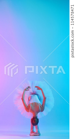 Ballerina in white tutu and bodysuit and pointe posing in tilt in neon light against vivid gradient background. Copy space. 114578471