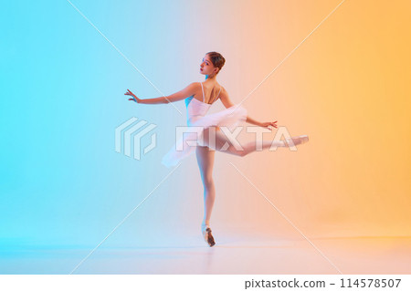 Young ballerina in white tutu doing arabesque in motion in neon light against blue-orange gradient background. Art through moves. 114578507