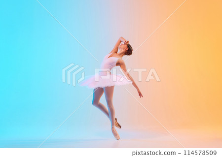Profile view of artistic ballerina dancing, leaning backwards elegantly in neon light against blue-orange gradient background. Profile view of artistic ballerina dancing, leaning backwards elegantly in neon light against blue-orange gradient background. 114578509