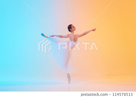 Elegant ballet dancer in white ensemble gracefully extends in neon light against blue-orange gradient background. 114578513
