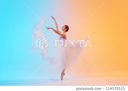 Talented young ballerina dancing in motion with fabric in neon light against blue-orange gradient background. Talented young ballerina dancing in motion with fabric in neon light against blue-orange gradient background. 114578515
