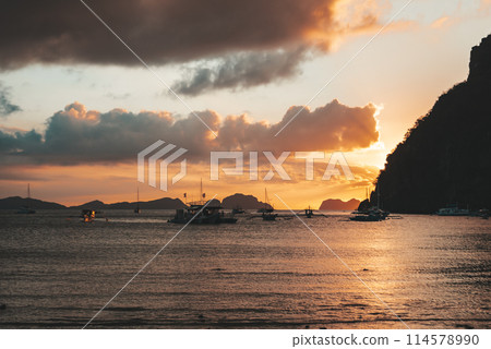 Boats anchored in a calm bay at sunset near scenic islands. Philippines, Palawan. Boats anchored in a calm bay at sunset near scenic islands. Philippines, Palawan. 114578990