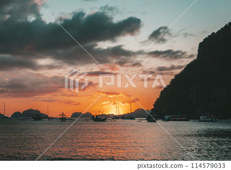 Boats anchored in a calm bay at sunset near scenic islands. Philippines, Palawan. Boats anchored in a calm bay at sunset near scenic islands. Philippines, Palawan. 114579033