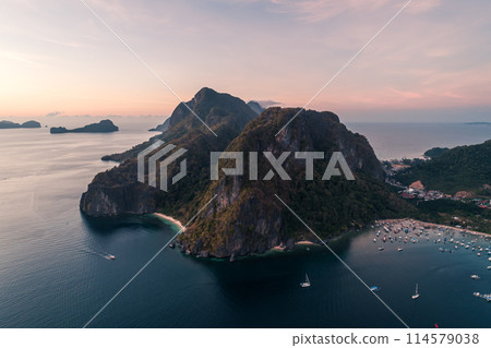 Aerial view of cliffs in the sea, yachts are sailing nearby, mountains covered with tropical forest. El Nido, Palawan, Philippines. 114579038