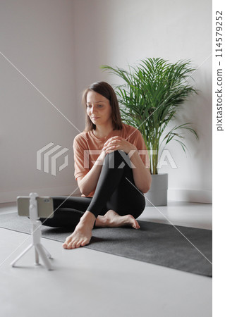 young Caucasian woman does sports online, stretches, practices yoga, meditation in gym young Caucasian woman does sports online, stretches, practices yoga, meditation in gym 114579252