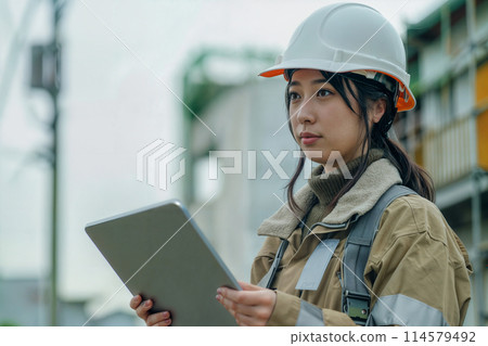 一名身穿工作服的婦女在建築工地操作平板電腦 114579492