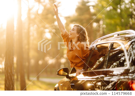 Beautiful traveler woman is resting and enjoying the sunset in the car. Active lifestyle, tourism. 114579668