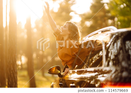 Beautiful traveler woman is resting and enjoying the sunset in the car. Active lifestyle, tourism. 114579669