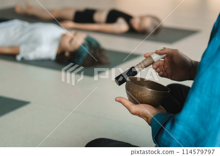 Children relax lying down to the sounds of a Tibetan bowl in the fitness room. Children's yoga 114579797