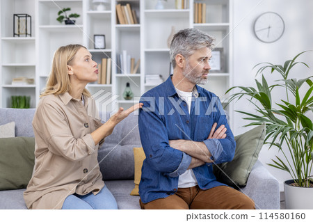 A couple engaged in a serious conversation at home, with the woman talking and the man looking away in silence. A couple engaged in a serious conversation at home, with the woman talking and the man looking away in silence. 114580160