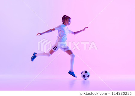 Dynamic image of teen girl, soccer player in white uniform in motion with ball against pink studio background in neon light 114580235