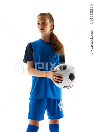 Teen girl in blue uniform, soccer player standing with ball, posing isolated on white studio background. Champion. 114580239