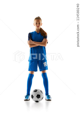 Focused teen girl in blue uniform, soccer player standing with ball, posing isolated on white studio background 114580240