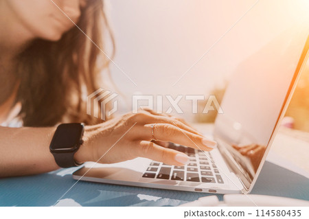 Woman laptop sea. Working remotely on seashore. Happy successful woman female freelancer working on laptop by the sea at sunset, makes a business transaction online. Freelance, remote work on vacation 114580435