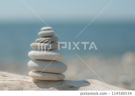 Balanced pebble pyramid on the beach on a sunny day. Abstract Sea bokeh on the background. Selective focus. Zen stones on the sea beach, meditation, spa, harmony, calmness, balance concept Balanced pebble pyramid on the beach on a sunny day. Abstract Sea bokeh on the background. Selective focus. Zen stones on the sea beach, meditation, spa, harmony, calmness, balance concept 114580534