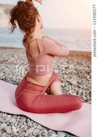 Middle aged well looking woman with black hair, fitness instructor in leggings and tops doing stretching and pilates on yoga mat near the sea. Female fitness yoga routine concept. Healthy lifestyle Middle aged well looking woman with black hair, fitness instructor in leggings and tops doing stretching and pilates on yoga mat near the sea. Female fitness yoga routine concept. Healthy lifestyle 114580577