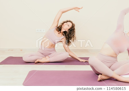 Well looking middle aged sporty woman, fitness instructor in pink sportswear doing stretching and pilates on yoga mat in the studio with mirror. Female fitness yoga. Healthy lifestyle and harmony. 114580615
