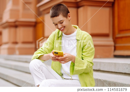 Portrait of woman with short haircut posing on city streets, with phone. Technology, style concept. 114581879