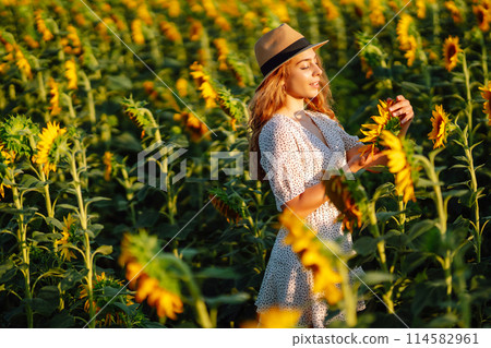 Sunny beautiful photo of happy woman, enjoying warm weather, walking in blooming sunflower field. 114582961