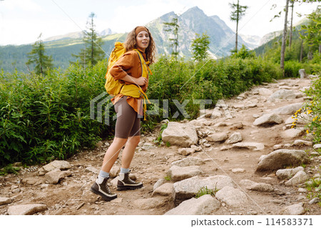 Young female traveler with hiking poles, bright backpack enjoys mountain scenery. Active lifestyle. Young female traveler with hiking poles, bright backpack enjoys mountain scenery. Active lifestyle. 114583371