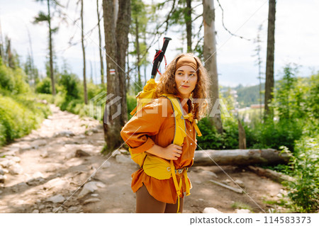 Young female traveler with hiking poles, bright backpack enjoys mountain scenery. Active lifestyle. 114583373
