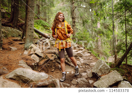 Smiling woman traveler along a forest hiking trail in the mountains against the backdrop of nature. 114583378